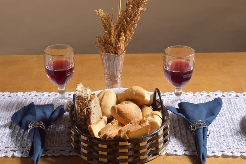 Mesa posta com cesta de pães, taças de vinho tinto e guardanapos azuis